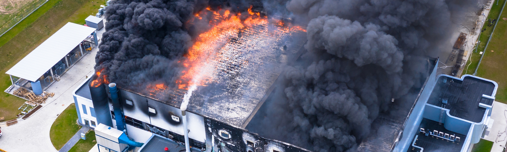 Aerial view of burnt industrial warehouse or logistics center building after big fire with huge smoke from burned roof