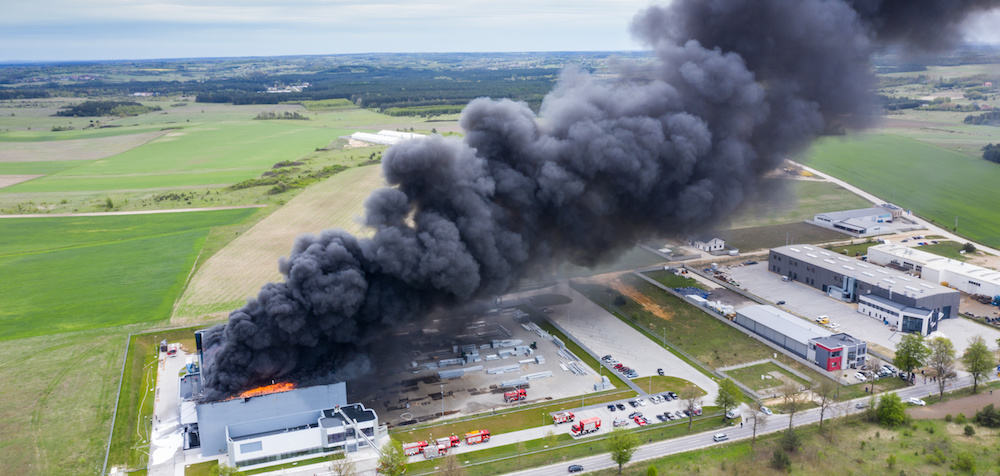 Aerial view of burnt industrial warehouse or logistics center building after big fire with huge smoke from burned roof